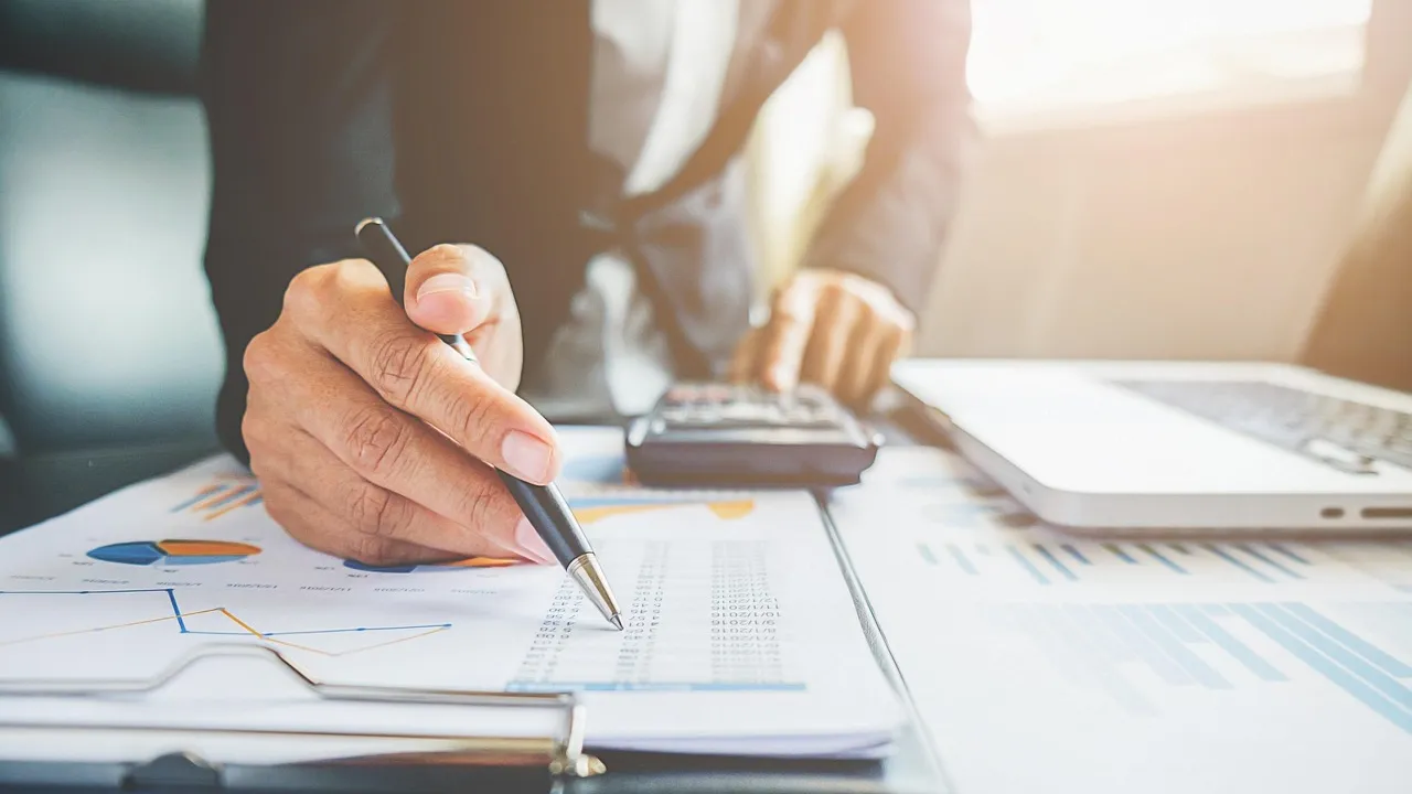 Hand met pen en rekenmachine boven een financieel overzicht